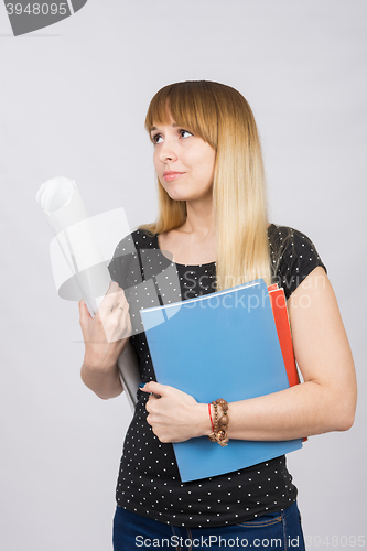 Image of Young girl student with folders and a roll of paper in his hand sadly looks aside