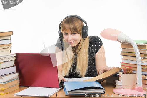 Image of Happy student with headphones sitting at the table and looking for the information you need in a laptop