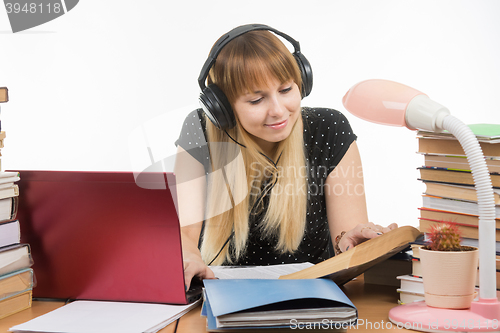 Image of Happy student sitting at the table and preparing for exams in headphones