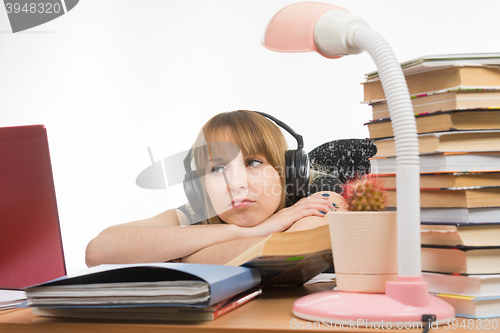 Image of Girl sad student sitting at the table wearing headphones and listening to music