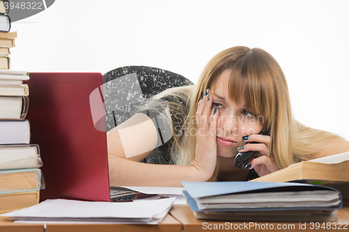 Image of Tired young woman office worker talking on the phone and looking at monitor