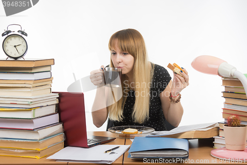 Image of Young teacher drinks coffee with a sandwich in the workplace