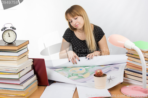 Image of Girl design student sitting at a desk and is tired deploys a large drawing