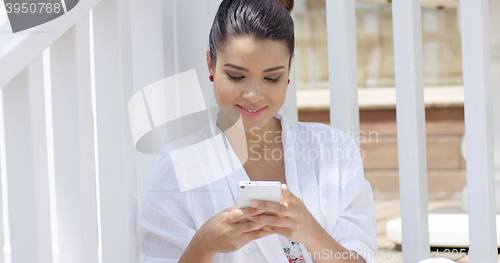 Image of Single woman sitting near fence using smart phone