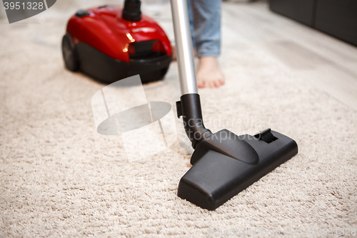 Image of Maid cleaning carpet with modern red vacuum cleaner