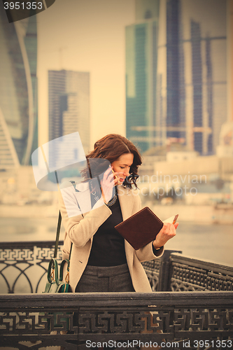 Image of woman in a bright coat with notebook talking on mobile