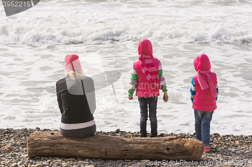 Image of Two girls and a girl on the beach sitting on a log and looking into the distance