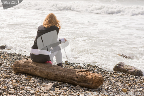 Image of Girl sitting on the log on the coast and looks at sea