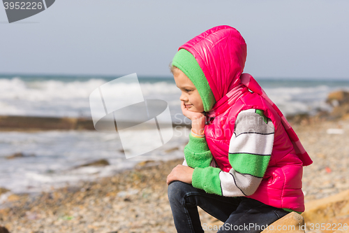 Image of Girl sitting on the rocky beach and the sea head on his hand looking to the frame