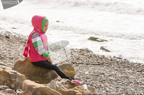 Image of Happy girl sitting on a rock on the sea coast and looking into the distance