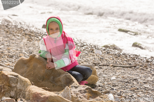 Image of Happy girl sitting on a rock on the sea coast and looking at the frame