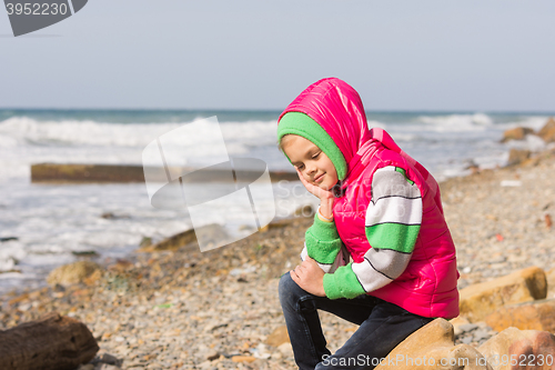 Image of Girl sitting on the rocky beach and the sea happily lost in thought looking down