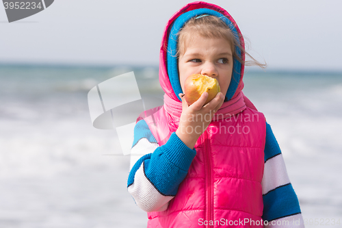 Image of Five-year girl eating an apple on the background of the sea coast