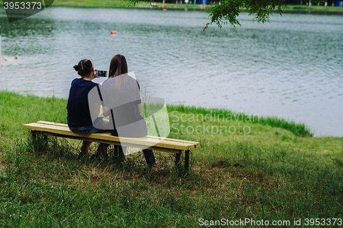 Image of Women sit on a bench and take selfies