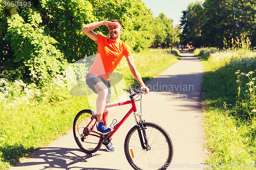 Image of happy young man riding bicycle outdoors