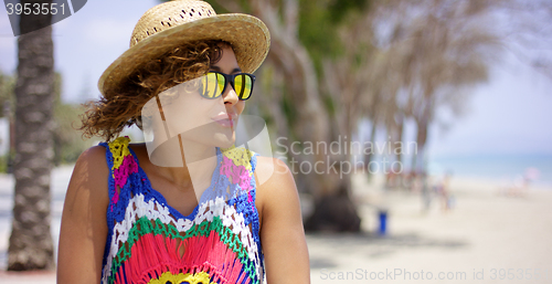 Image of Grinning woman in sunglasses and hat near ocean