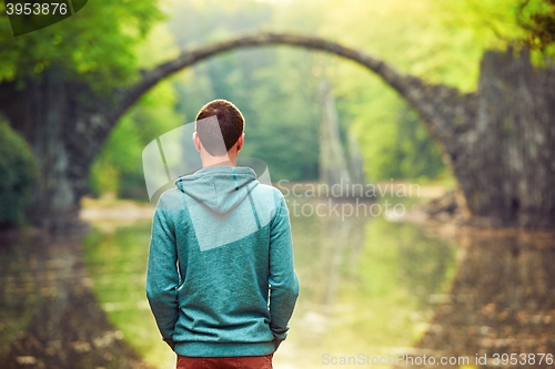 Image of Pensive man is looking at the old bridge