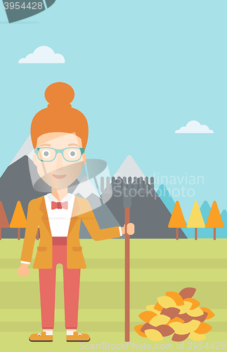 Image of Woman with rake standing near heap of autumn leaves.