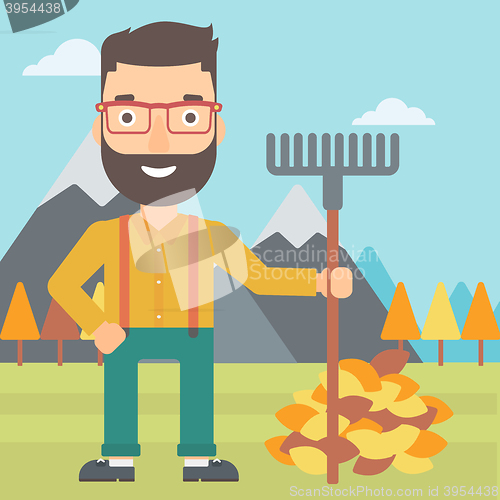 Image of Man with rake standing near heap of autumn leaves.