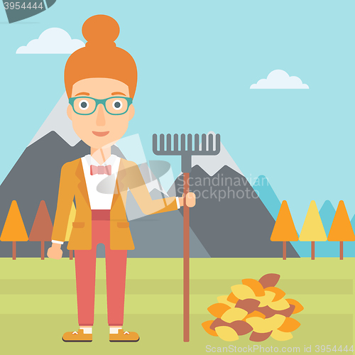 Image of Woman with rake standing near heap of autumn leaves.