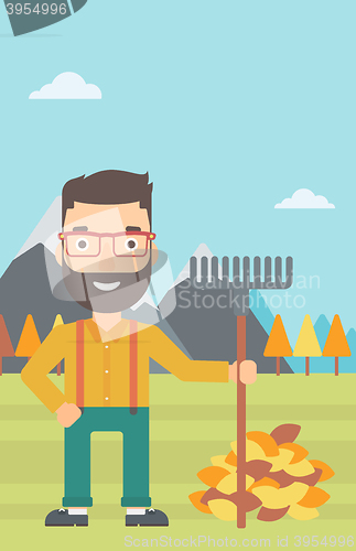 Image of Man with rake standing near heap of autumn leaves.