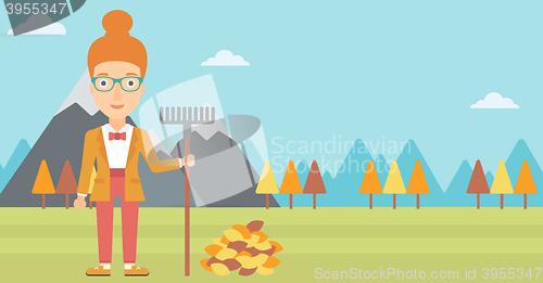 Image of Woman with rake standing near heap of autumn leaves.