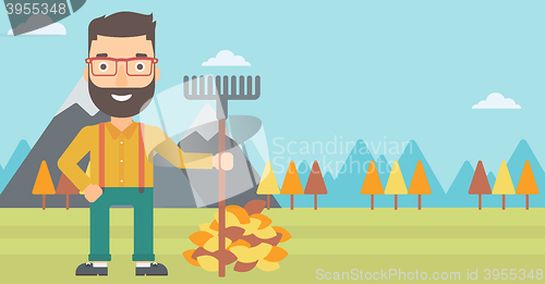 Image of Man with rake standing near heap of autumn leaves.