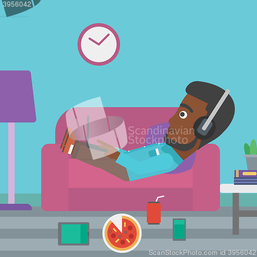 Image of Man lying on sofa with many gadgets.