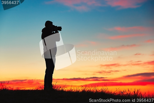 Image of Silhouette of young photographer is enjoying sun. Photographer at the sunrise