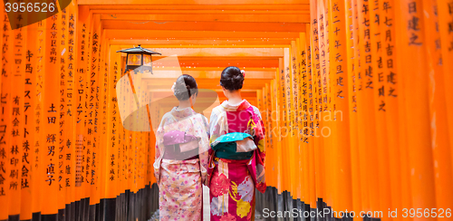 Image of Two geishas among red wooden Tori Gate at Fushimi Inari Shrine in Kyoto, Japan