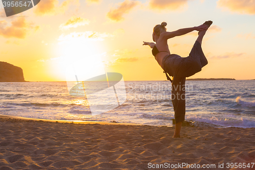 Image of Woman practicing yoga on sea beach at sunset.