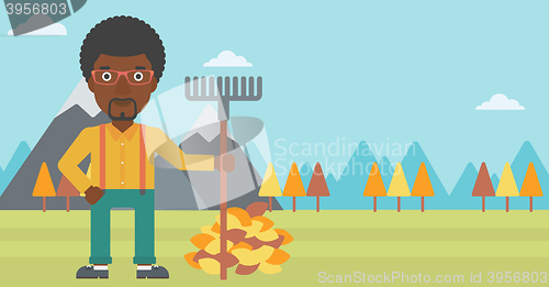 Image of Man with rake standing near heap of autumn leaves.