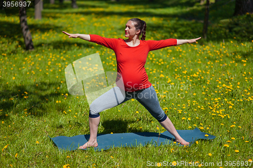 Image of Pregnant woman doing asana Virabhadrasana outdoors