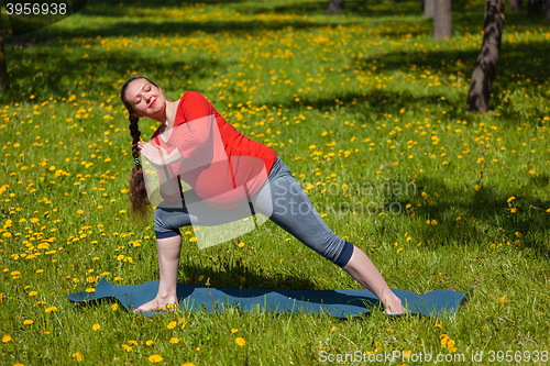 Image of Pregnant woman doing asana Utthita parsvakonasana outdoors