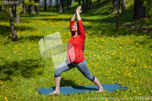 Image of Pregnant woman doing asana Virabhadrasana outdoors