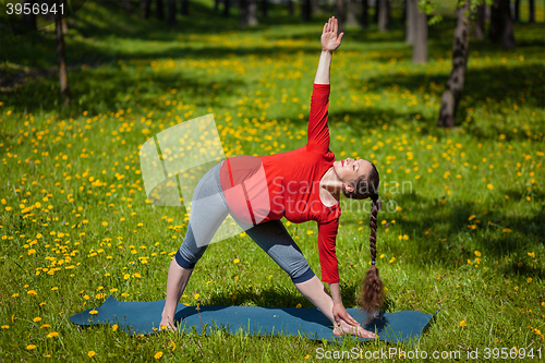 Image of Pregnant woman doing asana Utthita trikonasana outdoors