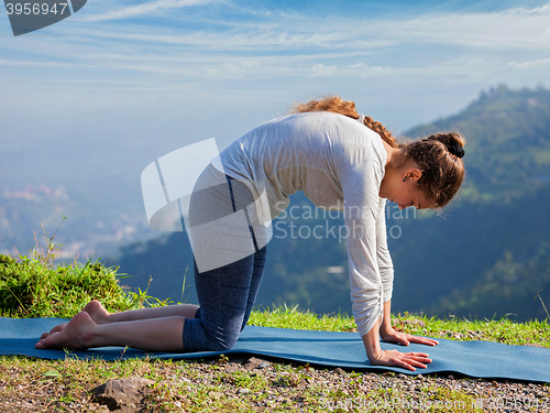 Image of Sporty fit woman practices yoga asana Marjariasana outdoors