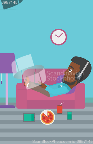 Image of Man lying on sofa with many gadgets.