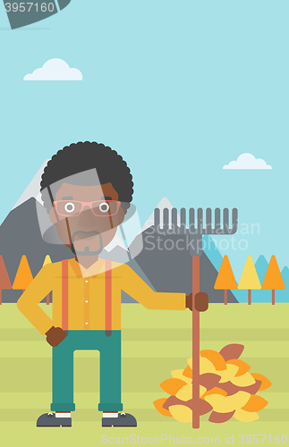 Image of Man with rake standing near heap of autumn leaves.