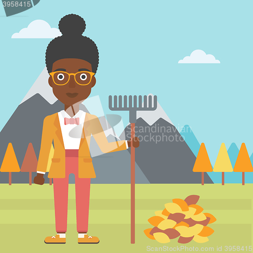 Image of Woman with rake standing near heap of autumn leaves.