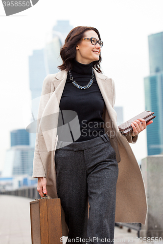 Image of smiling middle aged brunette in a bright coat and gray trousers 