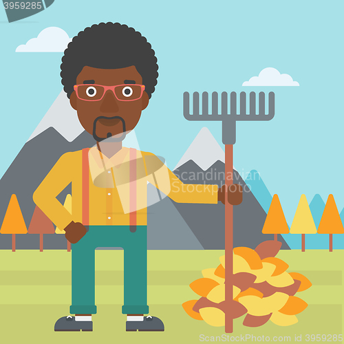 Image of Man with rake standing near heap of autumn leaves.