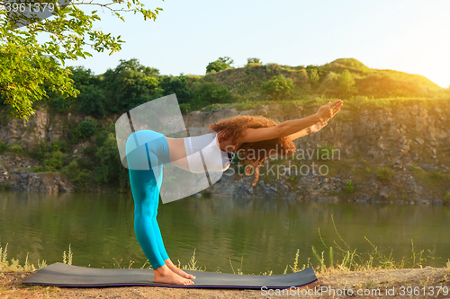 Image of Young woman is practicing yoga near river