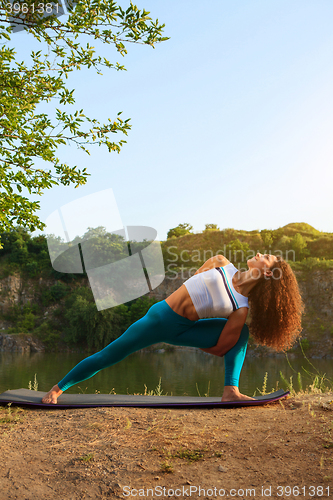 Image of Young woman is practicing yoga near river