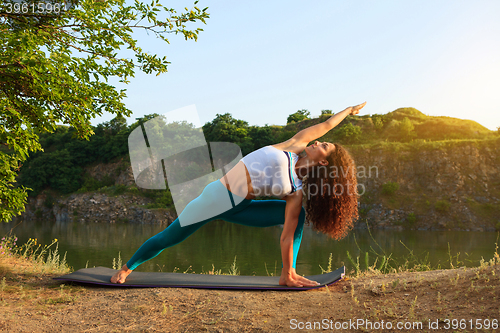 Image of Young woman is practicing yoga near river