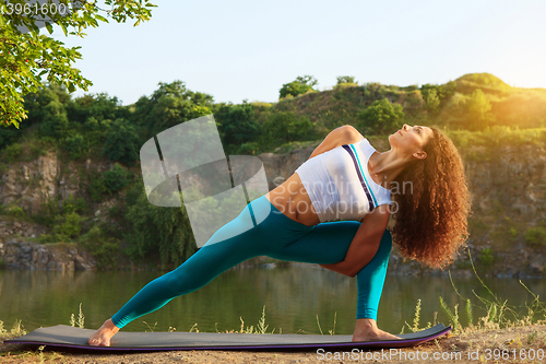 Image of Young woman is practicing yoga near river