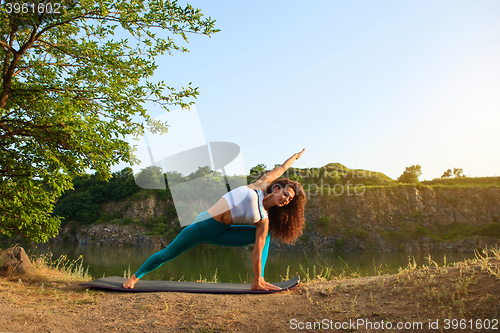 Image of Young woman is practicing yoga near river