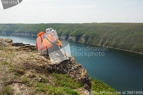 Image of Cyclist in Orange Wear Sitting on Rocky Hill