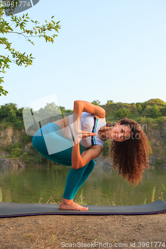 Image of Young woman is practicing yoga near river