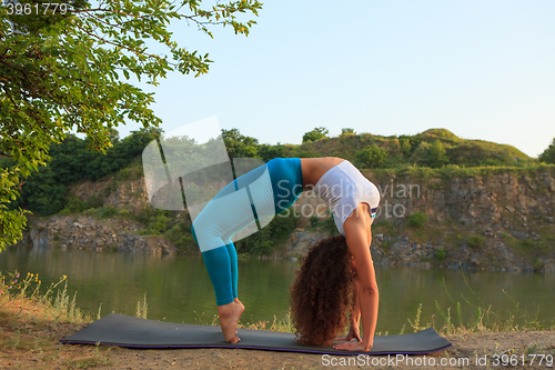 Image of Young woman is practicing yoga near river